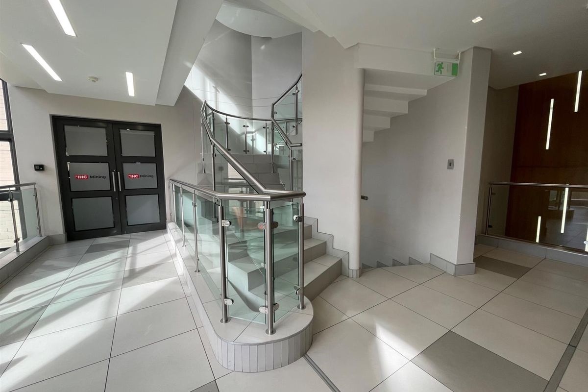 Modern office building entrance lobby featuring a prominent curved staircase with glass balustrades and clean, neutral tiled flooring.