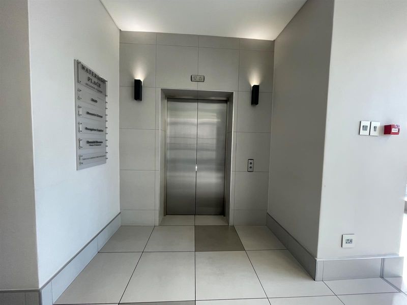 Modern office building elevator lobby featuring clean tiled flooring, stainless steel elevator doors, and professional directory signage.