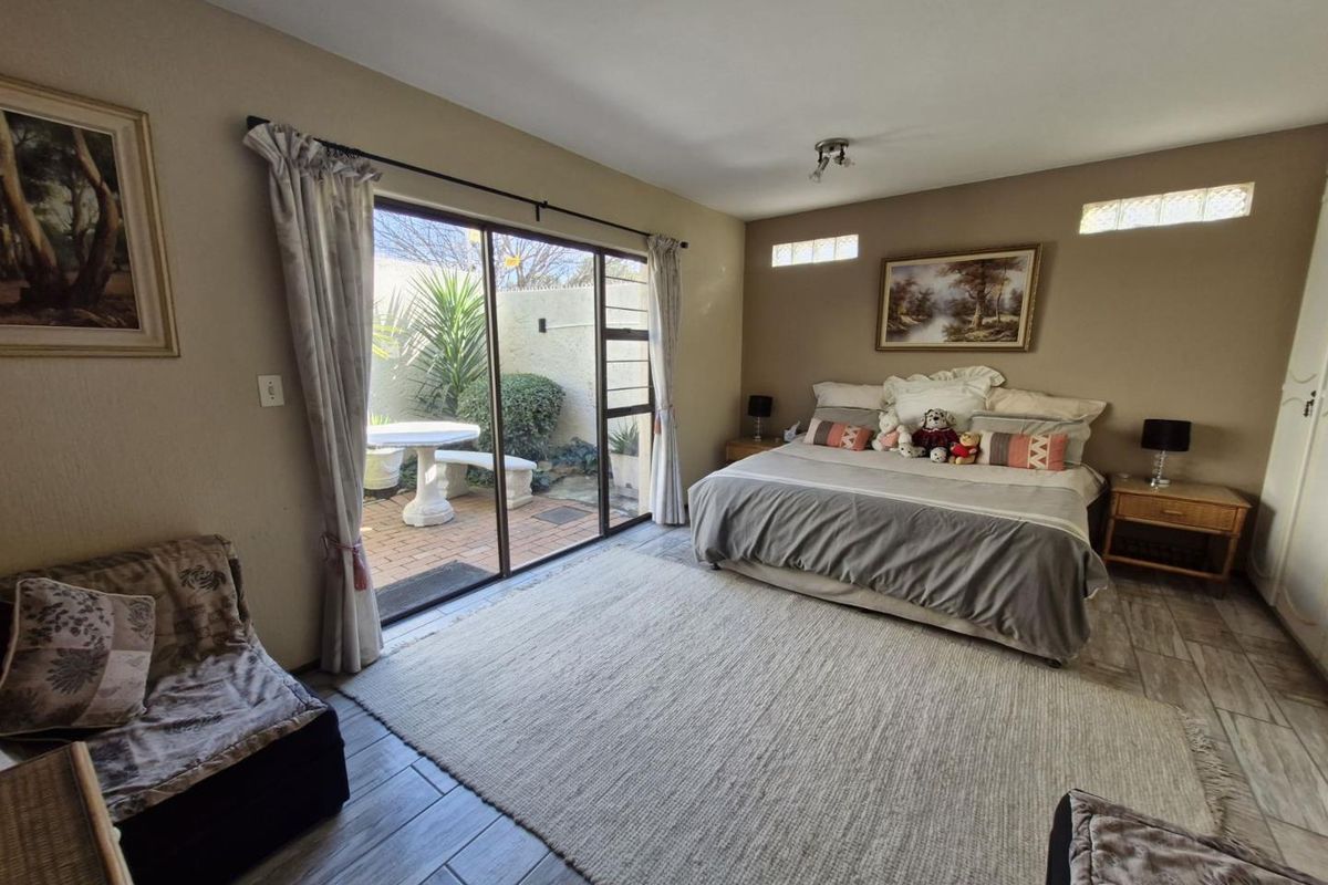 Spacious bedroom featuring tiled flooring, built-in cupboards, and large sliding glass doors providing direct access to a private paved patio area.