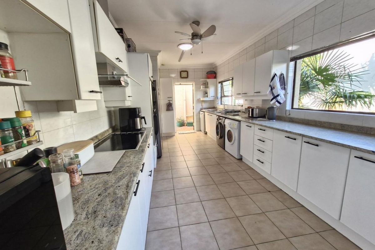A functional galley-style kitchen featuring white cabinetry, granite countertops, tiled flooring, and integrated laundry appliances.