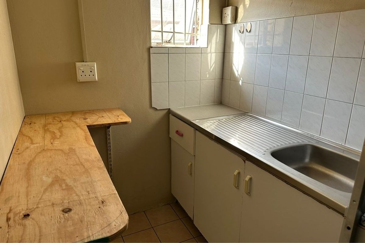A compact kitchenette featuring a stainless steel sink, tiled splashback, and basic built-in cabinetry with a plywood work surface.