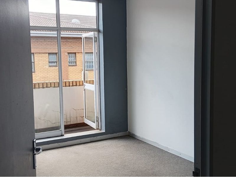 An empty office space featuring carpet flooring and direct access to a small balcony through an aluminium framed glass door.