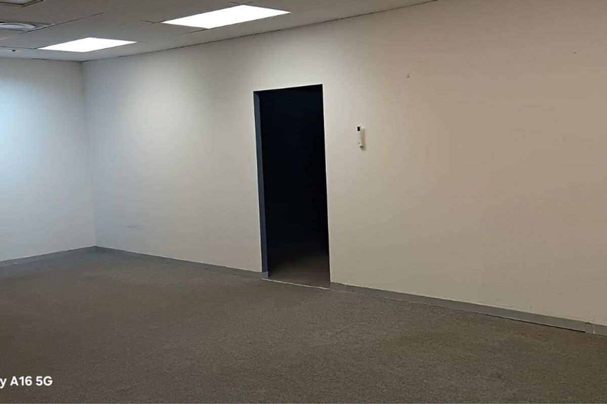 An empty, neutral-toned office space featuring recessed ceiling lighting and carpeted flooring, providing a blank canvas for professional workspace configuration.