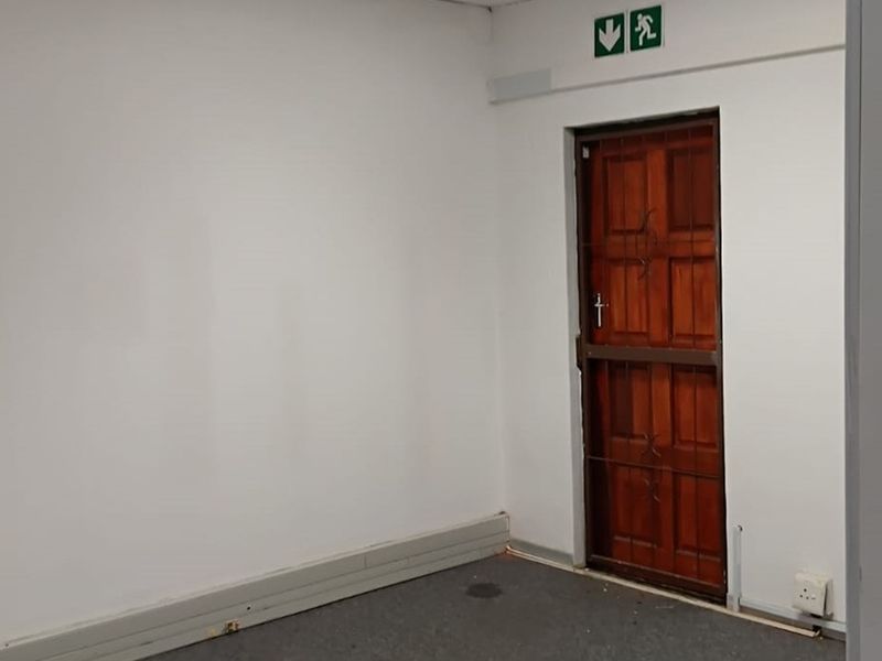 A vacant office space featuring a secure wooden door with a metal security gate and an emergency exit sign.