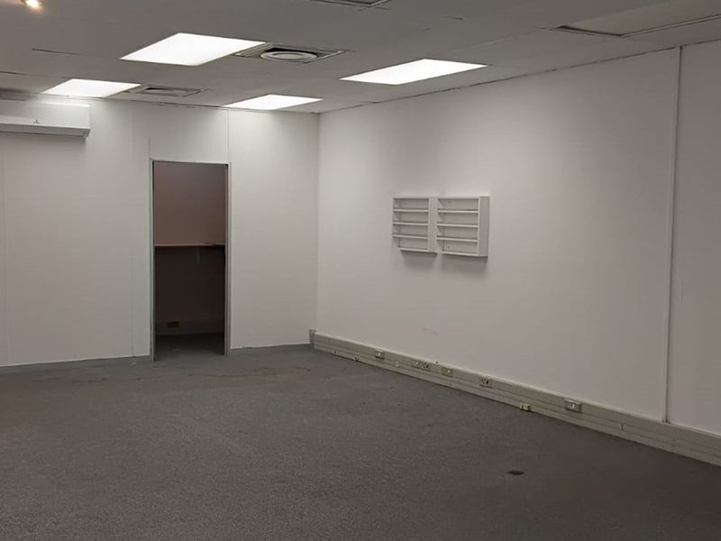 A vacant office space featuring neutral walls, carpeted flooring, recessed ceiling lighting, and a wall-mounted air conditioning unit.