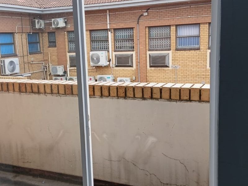 View from an office window overlooking a brick building facade with multiple external air conditioning units and a weathered boundary wall.