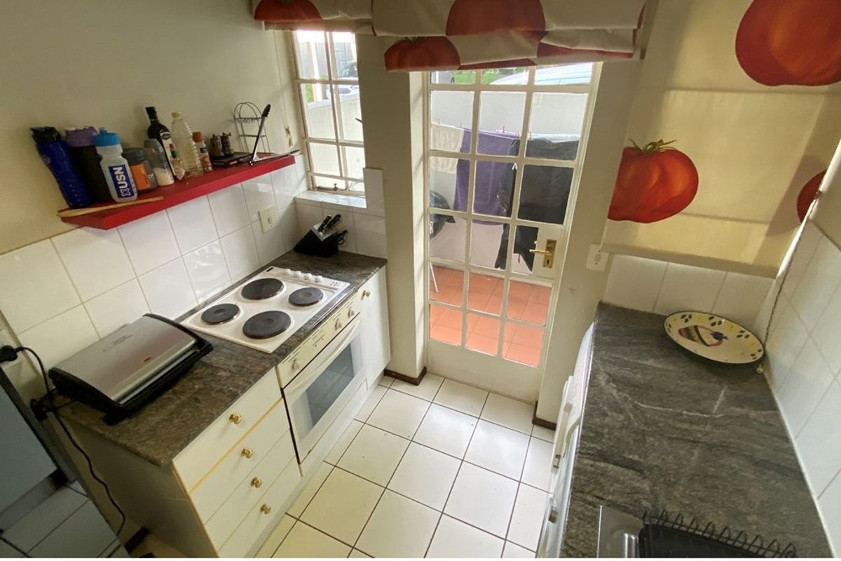 Compact kitchen featuring built-in cabinetry, electric hob, oven, and tiled flooring with direct access to an outdoor patio area.