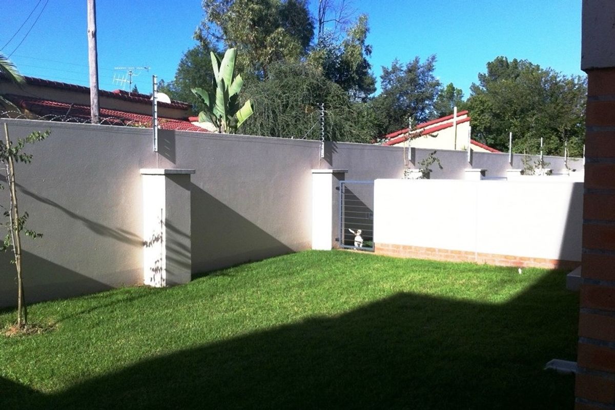 A private rear garden area featuring a well-maintained lawn, enclosed by high perimeter walls with integrated electric fencing and a secure metal gate.