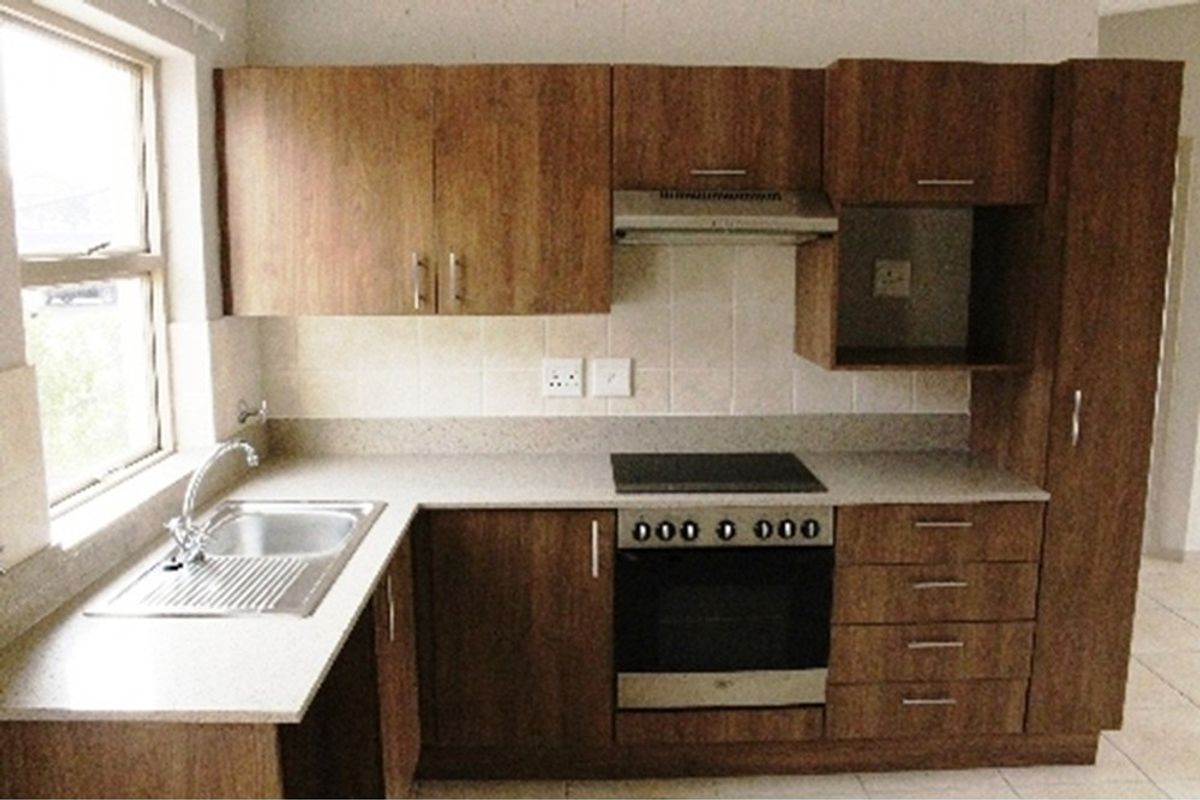 A functional kitchen featuring wood-look cabinetry, a built-in oven with hob, extractor fan, stainless steel sink, and tiled flooring.