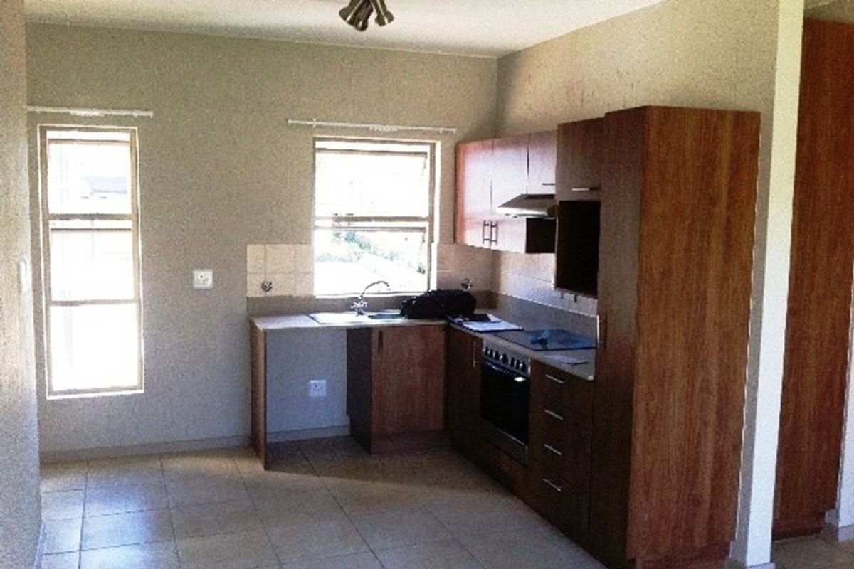 A functional kitchen featuring wood-finish cabinetry, built-in oven and hob, tiled flooring, and a stainless steel sink with a window view.