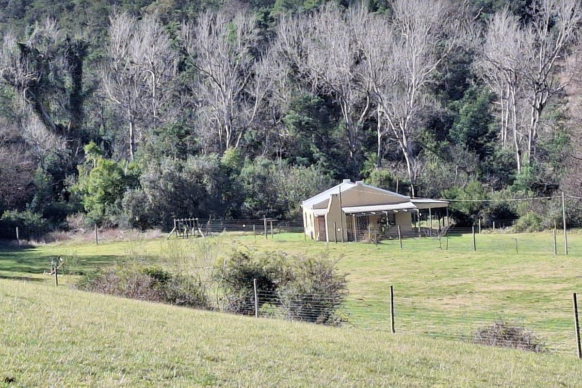 A view of a rural farm cottage nestled against a backdrop of mature trees and rolling hills.