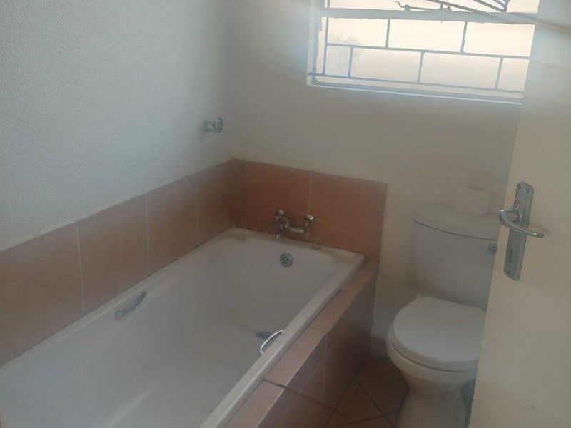 A functional bathroom featuring a built-in bathtub with tiled surround, a standard toilet, and a window with security bars.