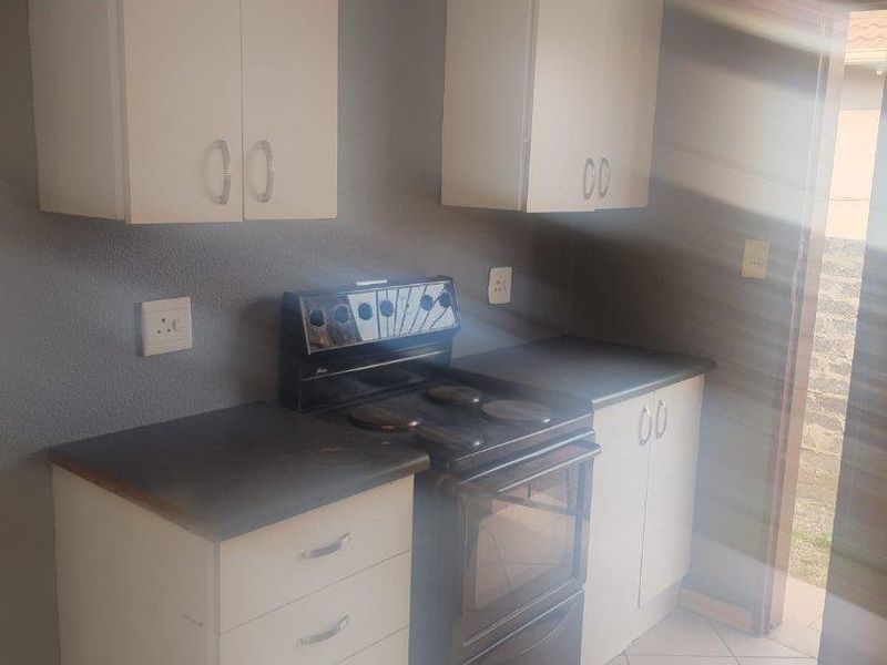 Compact kitchen featuring white cabinetry, dark countertops, and a freestanding electric stove, with direct access to an outdoor area.