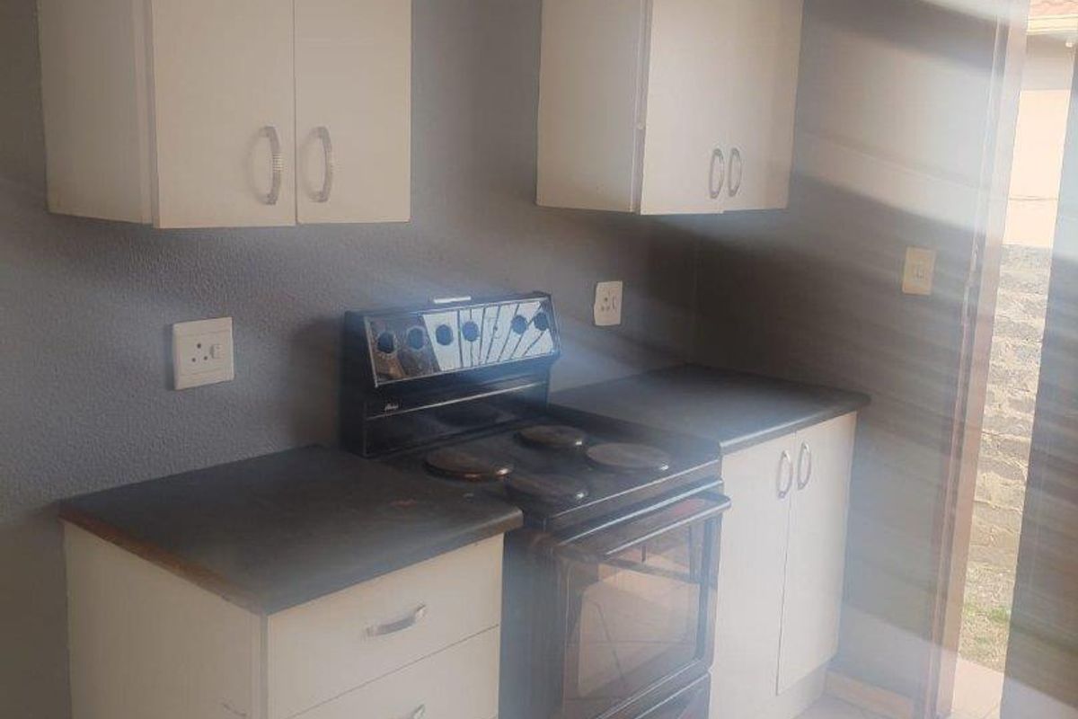 Compact kitchen featuring white cabinetry, dark countertops, and a freestanding electric stove, with direct access to an outdoor area.