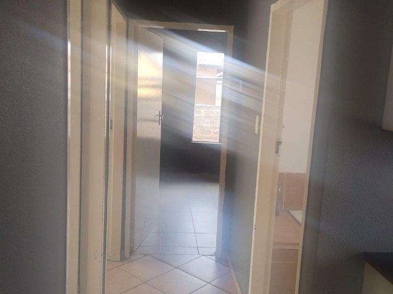 A functional interior hallway featuring tiled flooring and access to multiple rooms, characterized by natural light entering from the rear.