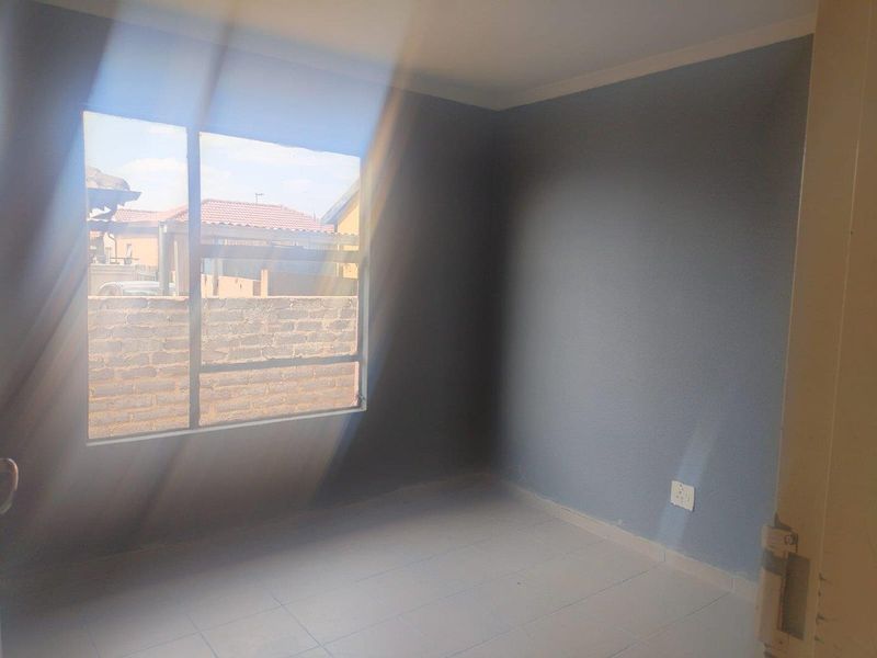 A vacant bedroom featuring tiled flooring, grey painted walls, and a large window allowing natural light.