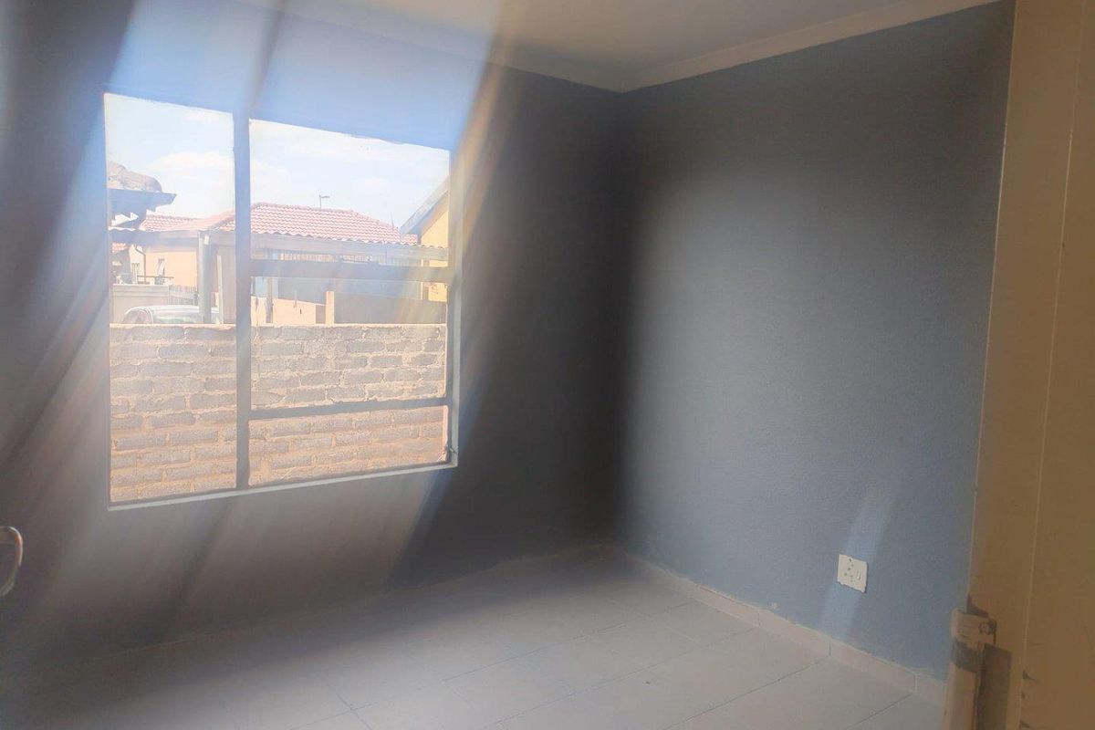 A vacant bedroom featuring tiled flooring, grey painted walls, and a large window allowing natural light.