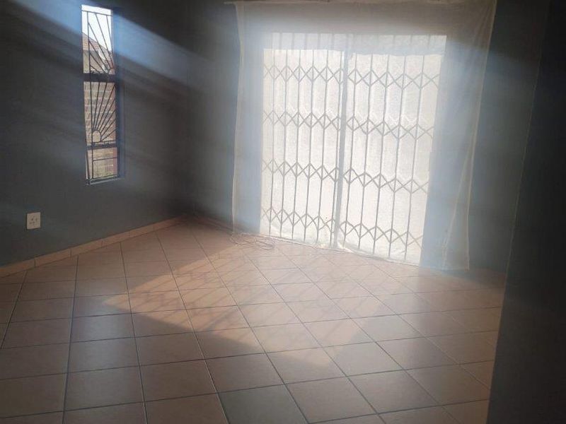 An empty living room featuring tiled flooring, dark-toned walls, and a sliding glass door secured with a metal security gate.