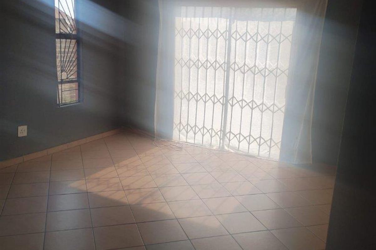 An empty living room featuring tiled flooring, dark-toned walls, and a sliding glass door secured with a metal security gate.