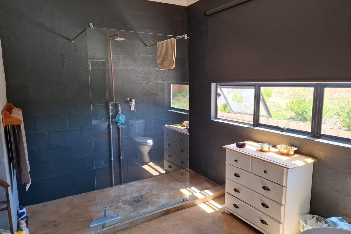 Modern bathroom featuring a walk-in glass shower enclosure, dark painted block walls, and large windows providing natural light.