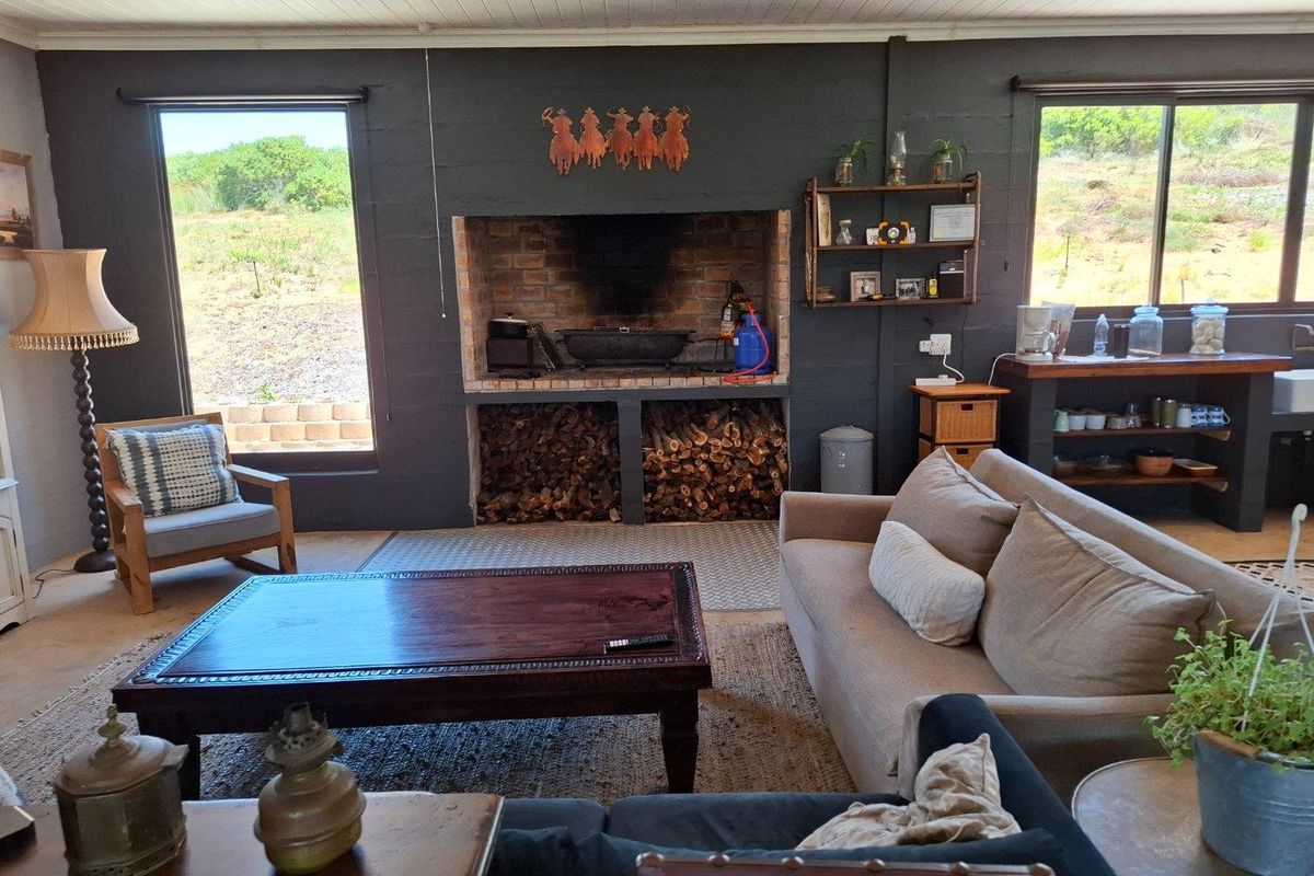 A rustic living room featuring a large built-in brick fireplace with integrated wood storage, dark painted block walls, and large windows overlooking the landscape.