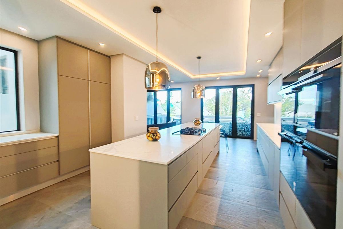 Modern kitchen featuring a large central island with stone countertops, integrated cabinetry, built-in oven, and recessed ceiling lighting with a sleek, contemporary finish.