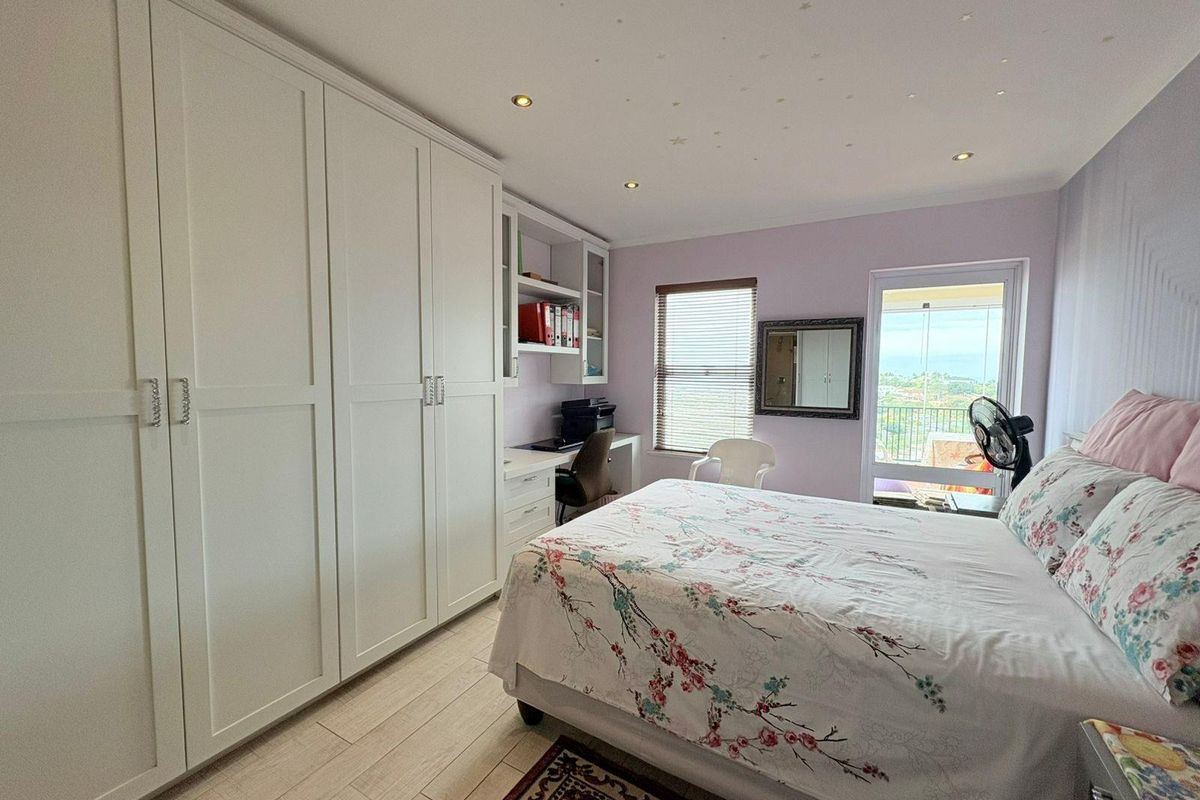 A well-maintained bedroom featuring extensive built-in cabinetry, a dedicated integrated desk workspace, recessed ceiling lighting, and direct access to a private balcony.