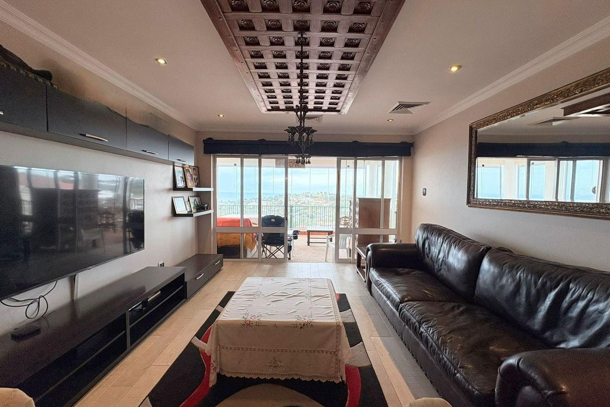Spacious living room featuring a decorative coffered ceiling, recessed lighting, and large sliding glass doors leading to a balcony with scenic views.