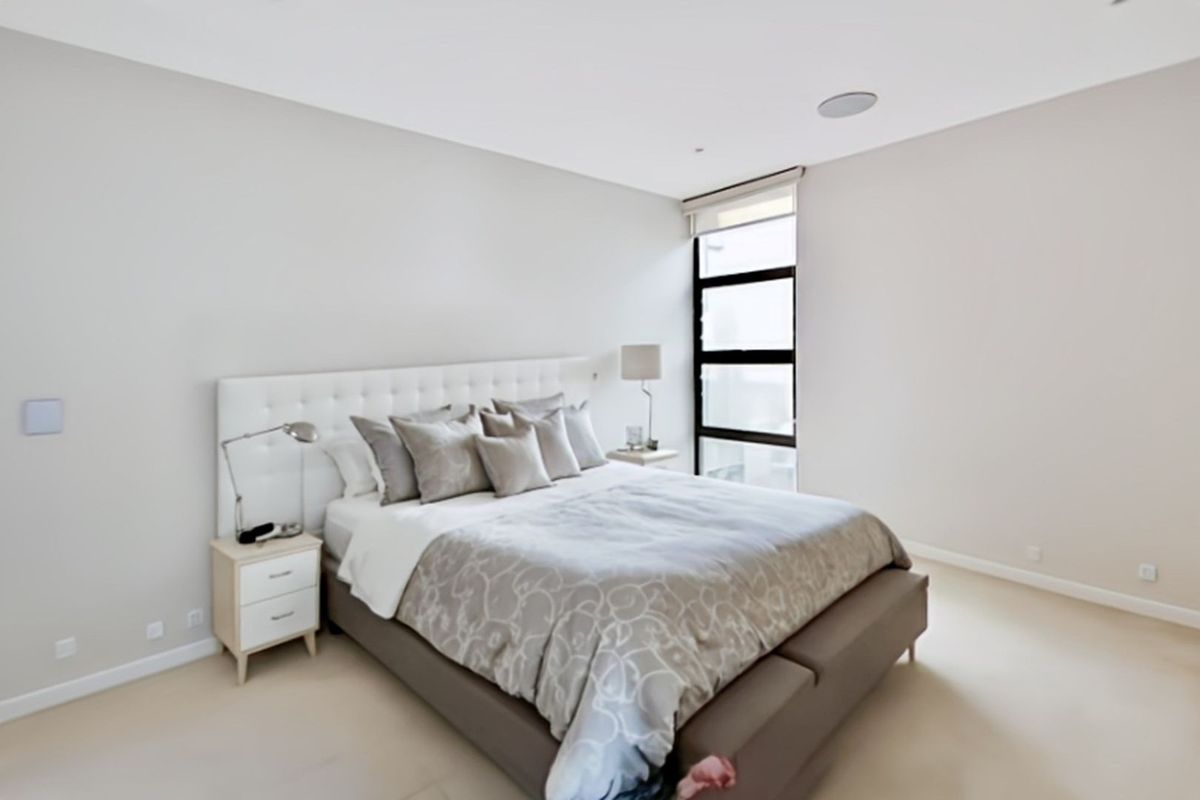 A bright and modern bedroom featuring neutral tones, recessed ceiling lighting, and a large window providing natural light.
