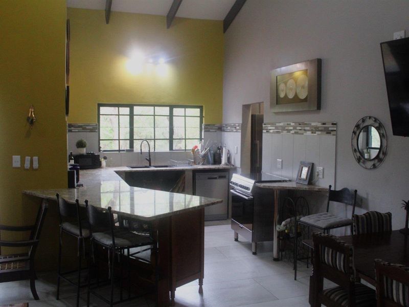 Open plan kitchen featuring granite countertops, a central island, tiled flooring, and exposed ceiling beams, creating a functional and connected living space.