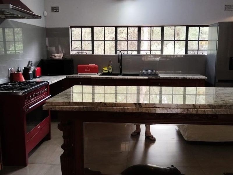 Spacious kitchen featuring granite countertops, a gas stove with extractor fan, double sink, and exposed ceiling beams with tiled flooring.