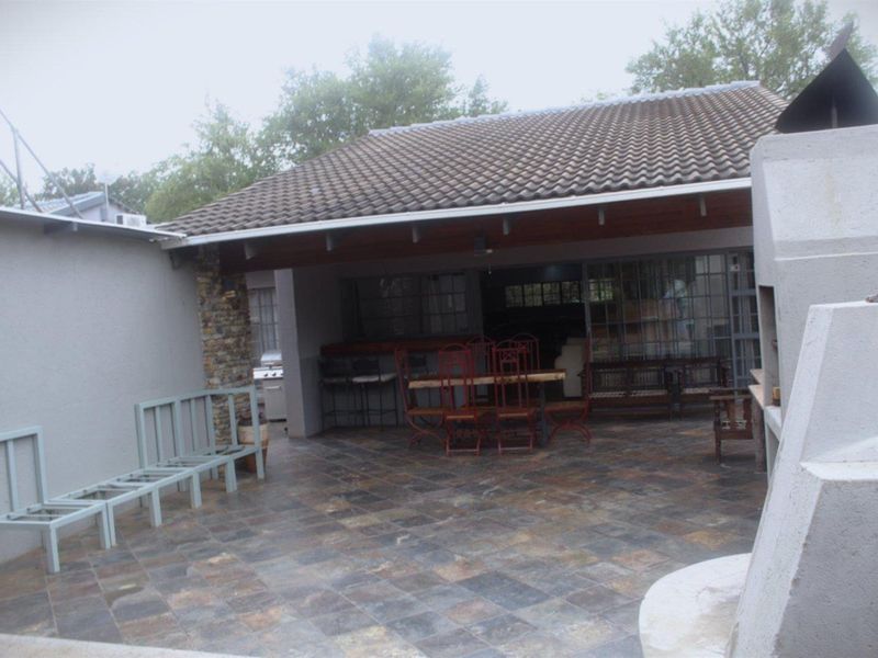 Covered outdoor patio area featuring tiled flooring, stone cladding accents, and a built-in braai, providing a functional space for outdoor entertaining.
