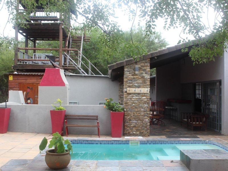 Outdoor entertainment area featuring a swimming pool, covered patio, built-in braai, and a unique raised wooden viewing deck structure.