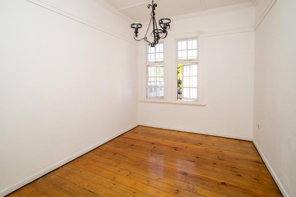 An empty room featuring polished timber flooring, high ceilings with decorative molding, and classic multi-pane windows.