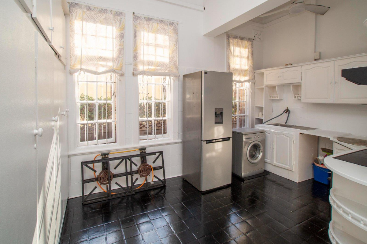 A functional kitchen area featuring white cabinetry, dark tiled flooring, large windows, and integrated space for laundry appliances.