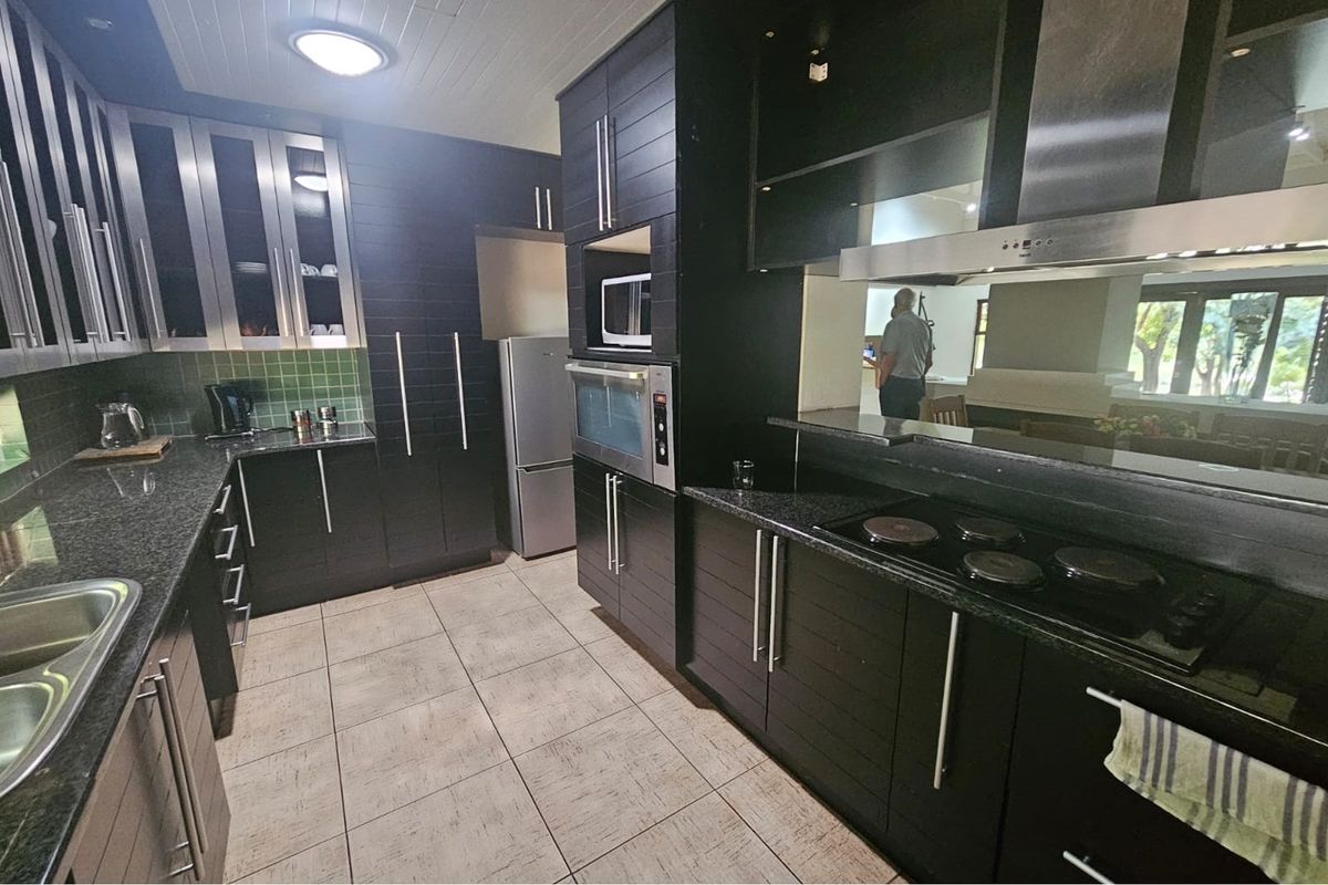 Modern kitchen featuring dark cabinetry, granite countertops, tiled flooring, built-in oven, microwave, and a stainless steel extractor fan.