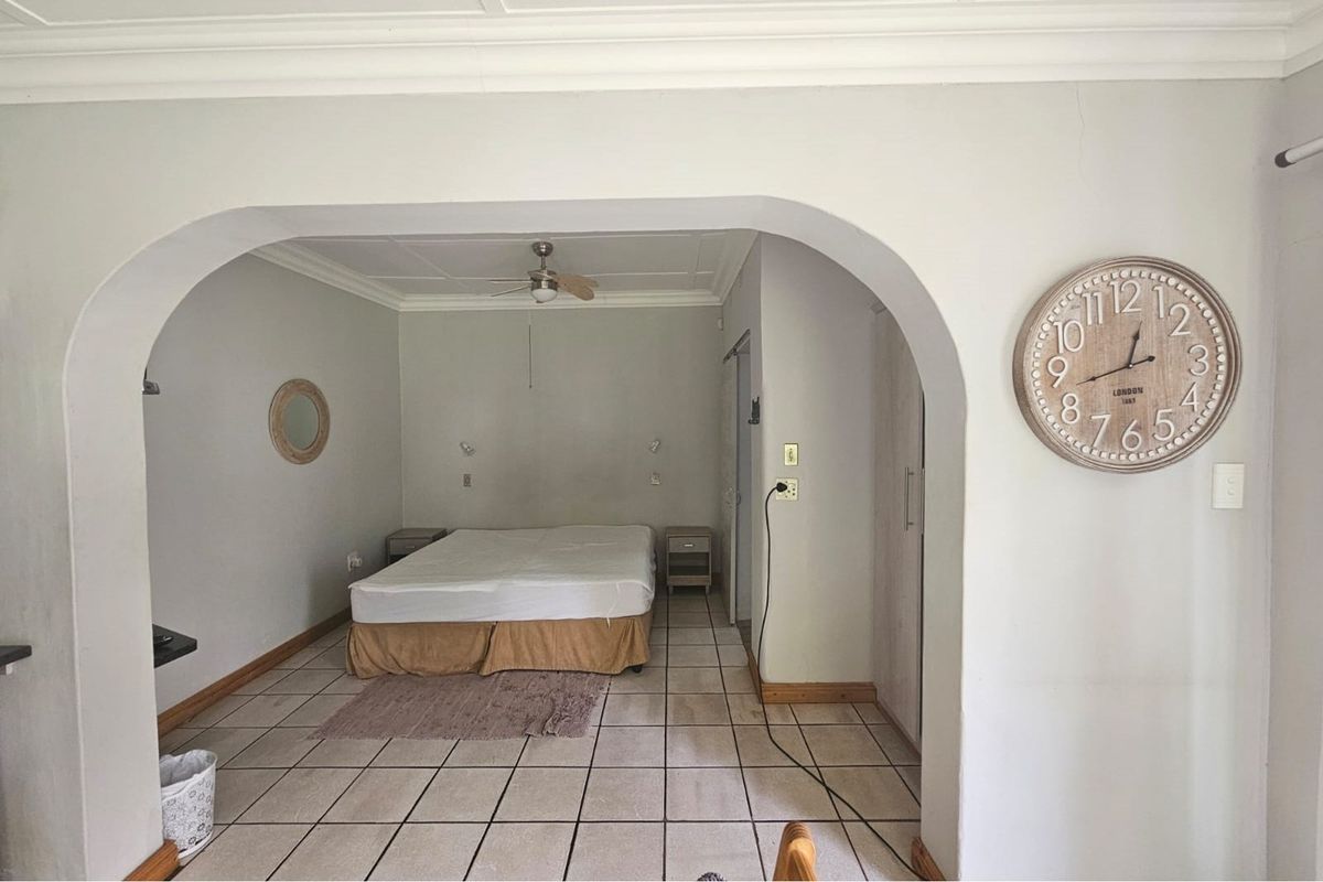 A bedroom featuring tiled flooring, a ceiling fan, and an arched entryway, providing a functional and simple sleeping space.