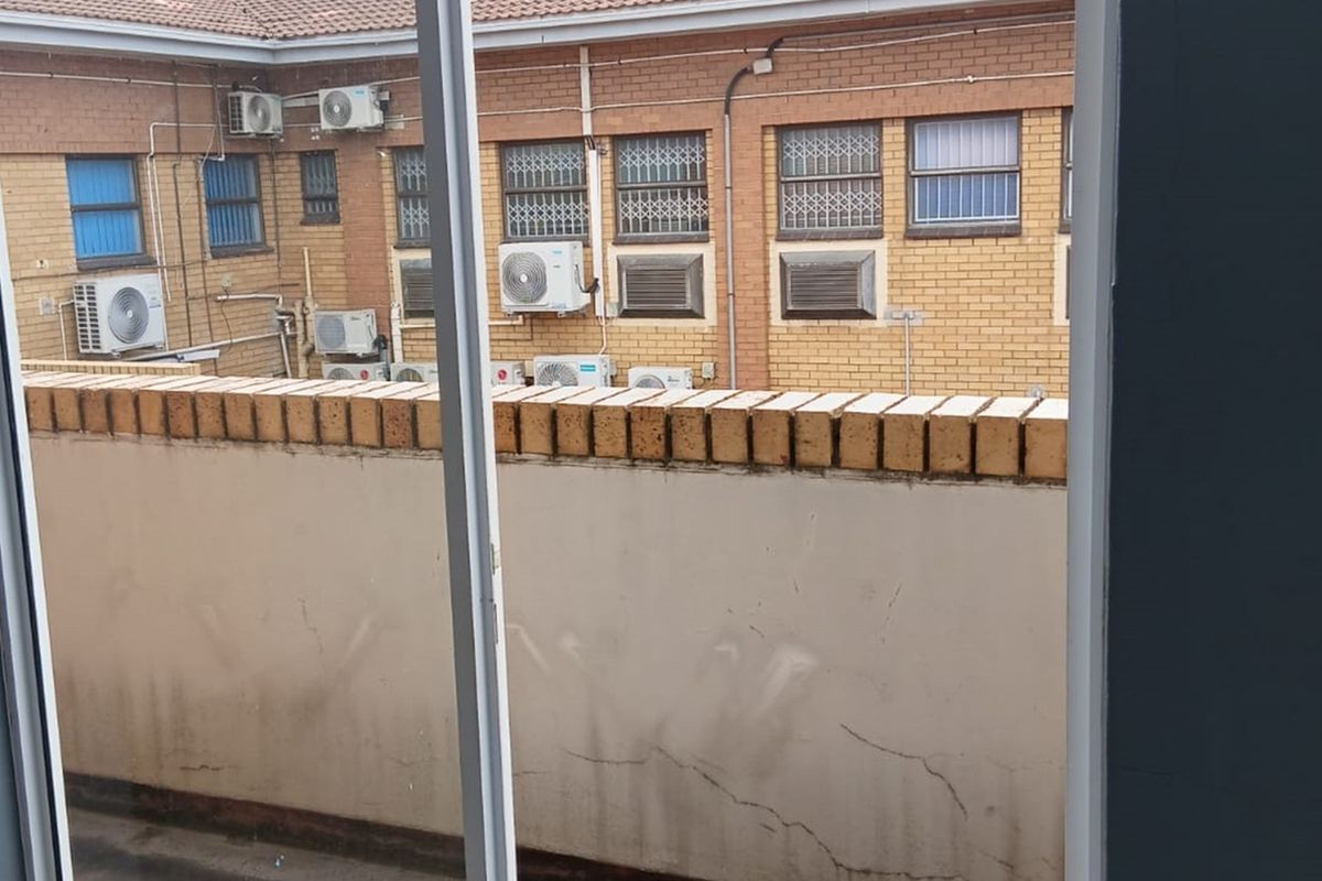 View of a rear exterior area featuring a brick boundary wall with visible cracking and multiple wall-mounted air conditioning units on the adjacent building facade.