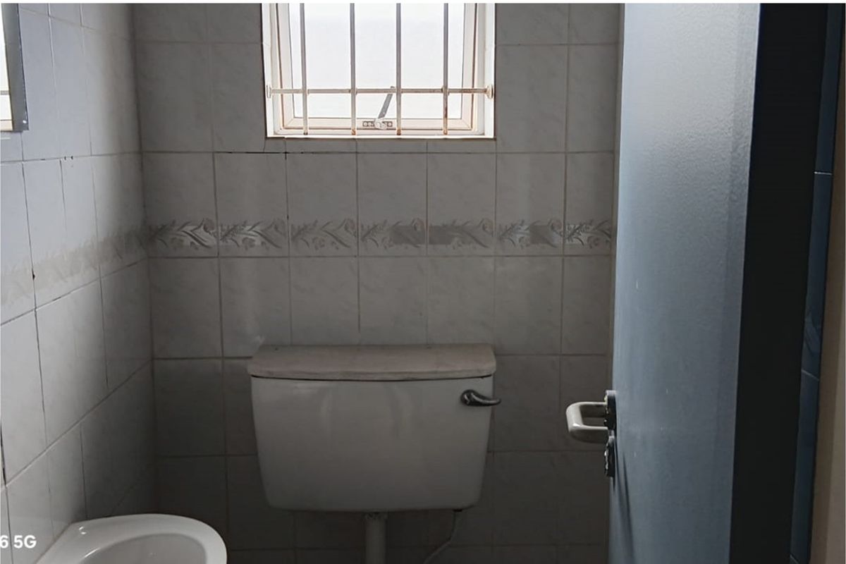 A functional bathroom space featuring ceramic wall tiling, a window with security bars, and a standard toilet cistern.