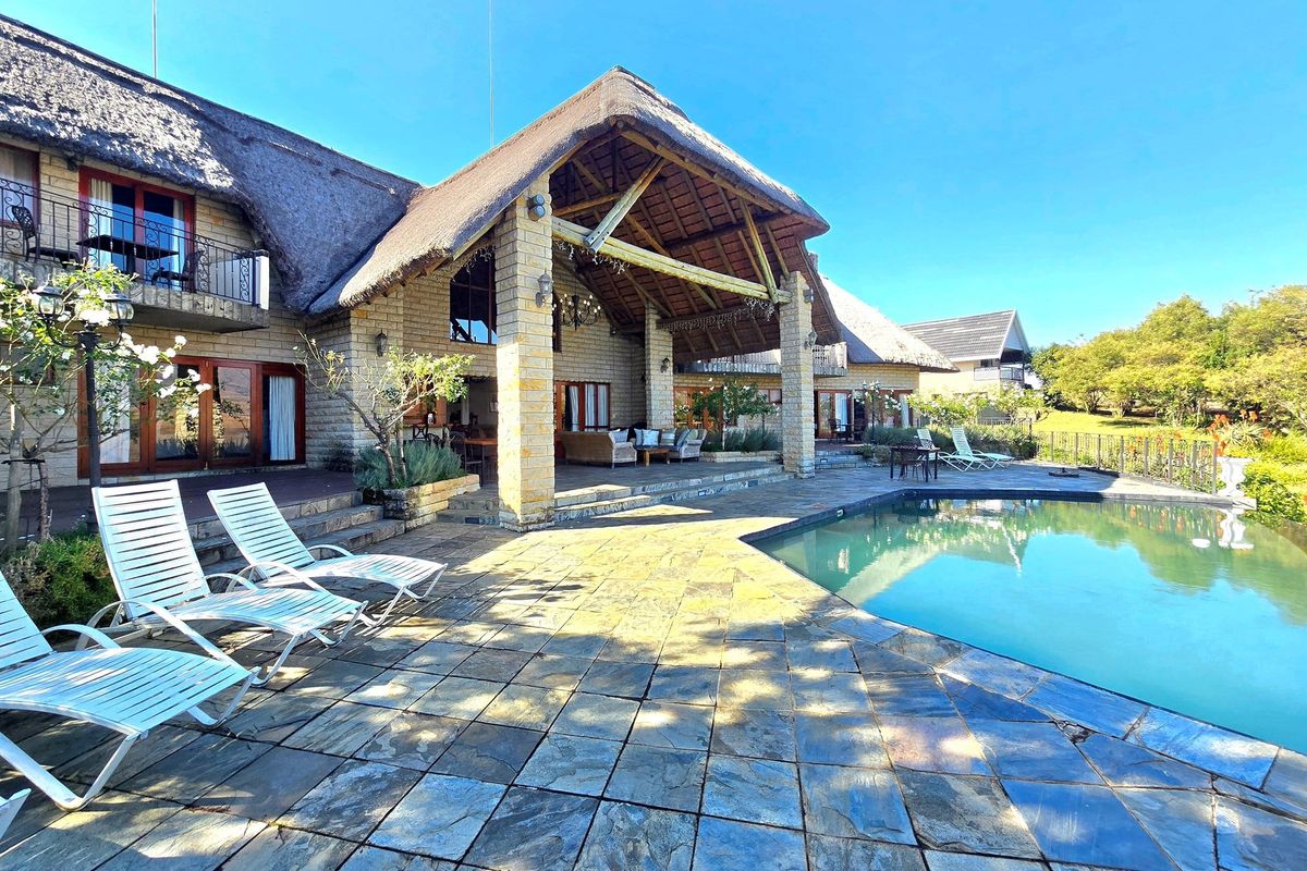 Spacious rear patio area featuring a thatched roof, stone paving, and a swimming pool, ideal for outdoor entertaining.