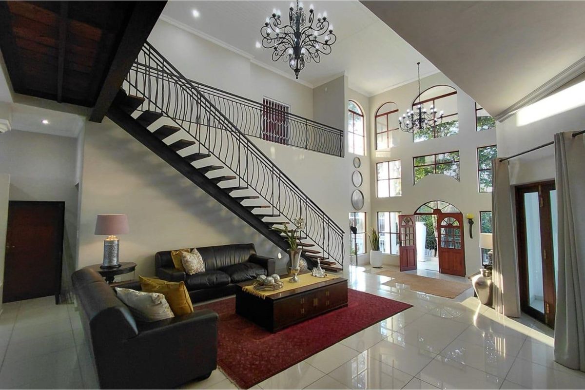 Spacious double-volume living area featuring a grand staircase with wrought iron balustrade, large arched windows, and polished tile flooring.