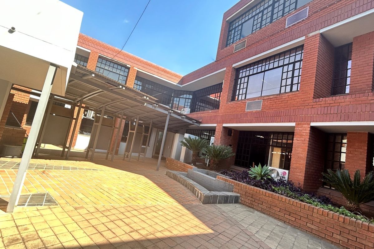 A view of the office building exterior featuring red brick facade, paved courtyard, and a covered walkway.