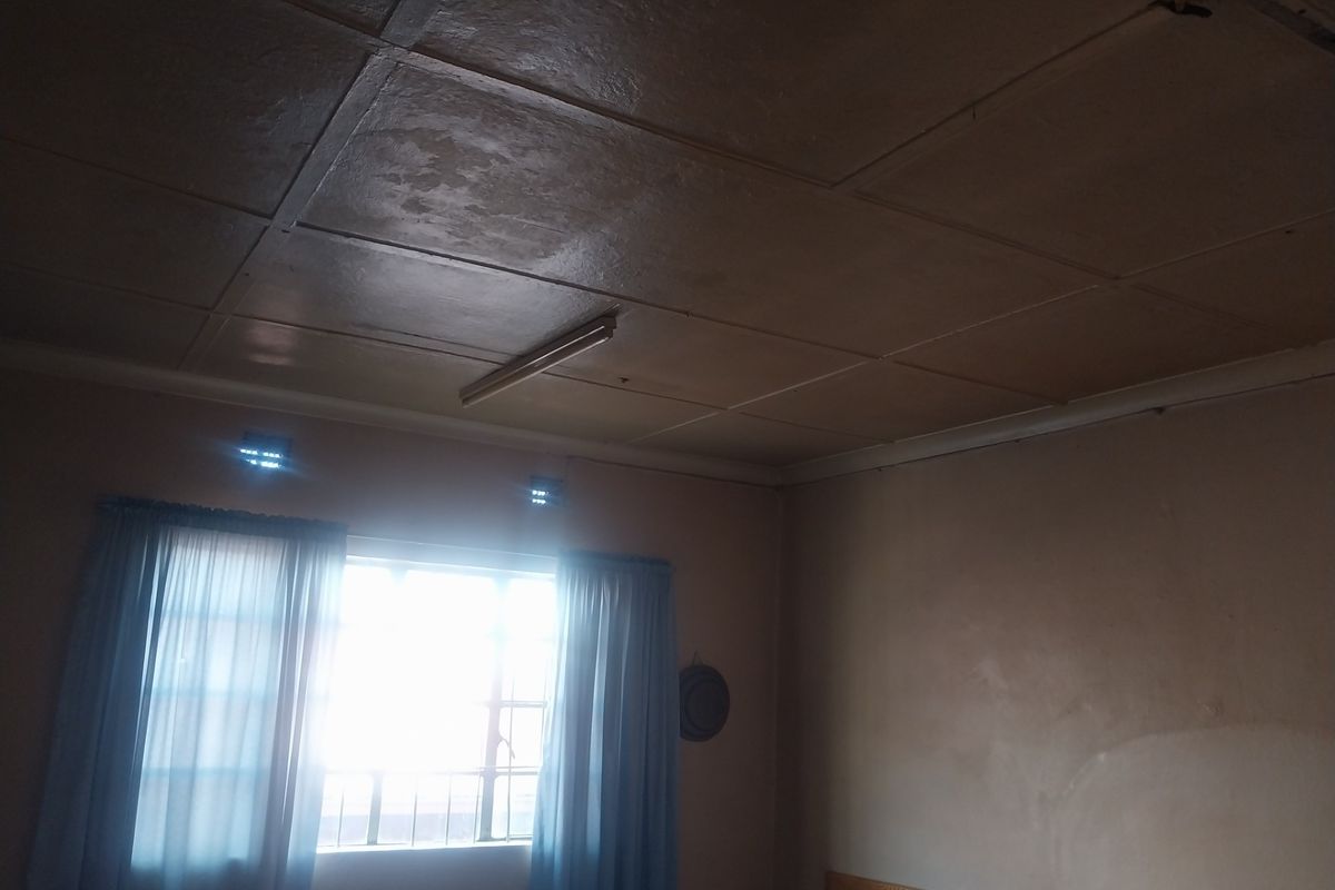 A bedroom featuring a panelled ceiling, a window with natural light, and basic wall finishes, requiring cosmetic updates.