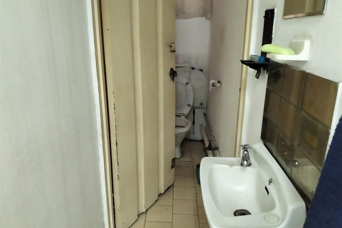 A compact bathroom featuring a wall-mounted basin, tiled splashback, and a separate toilet area accessed through a folding door.
