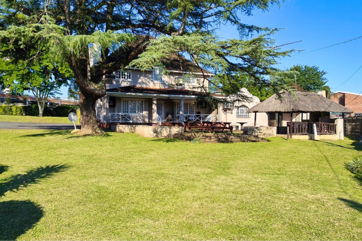 Rear view of the property featuring a spacious lawn, a covered patio area, and a traditional thatched lapa structure.