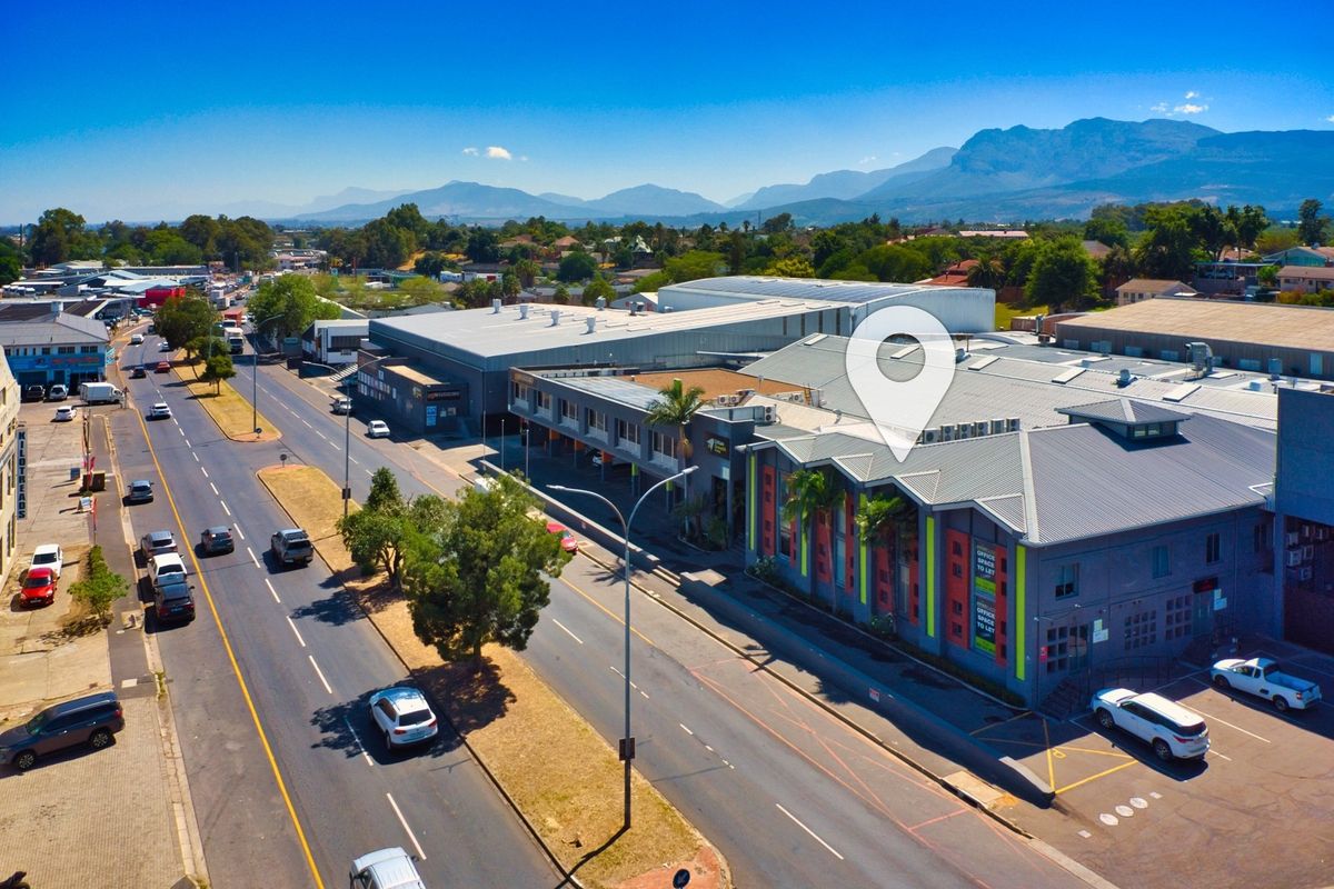 Aerial view of a commercial retail property complex situated along a main road, featuring modern metal roofing and integrated parking facilities.