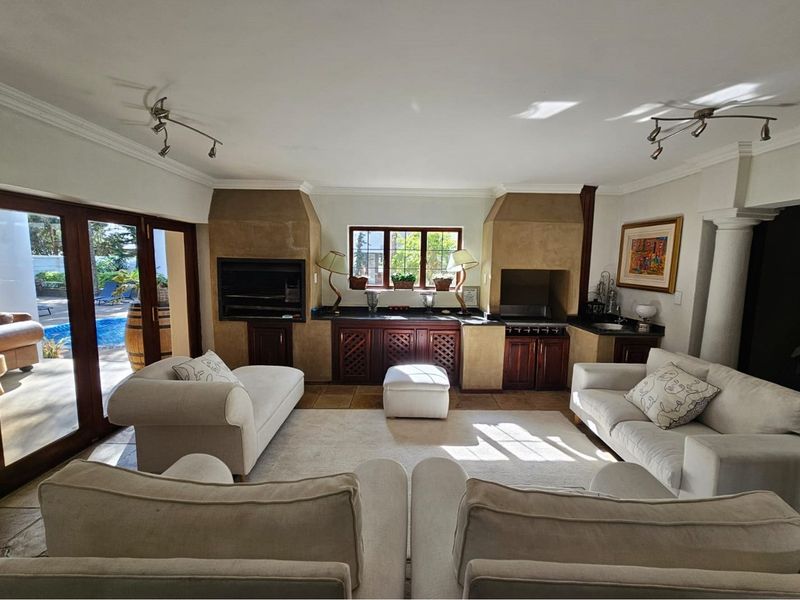 Spacious open-plan living area featuring a built-in indoor braai, stone-finish fireplace surrounds, dark wood cabinetry, and large glass doors opening to the pool area.