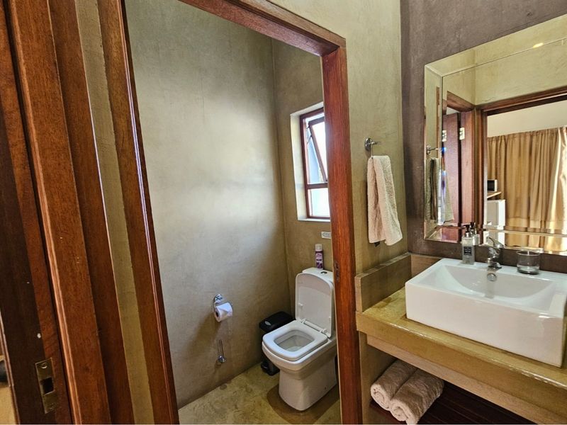 A functional bathroom featuring a modern vessel sink on a concrete-style vanity, a separate toilet area, and a wall-mounted mirror.