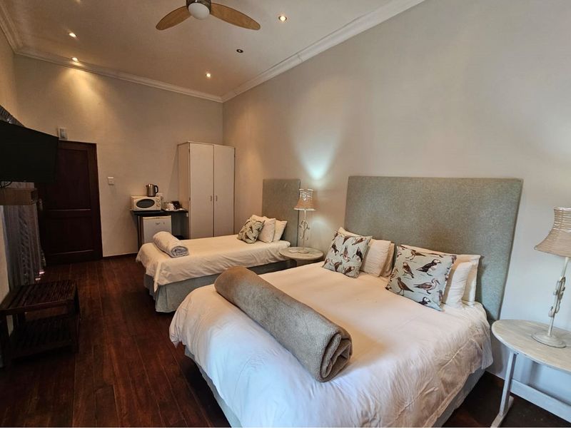 A well-maintained guest bedroom featuring dark wood flooring, recessed ceiling lighting, a ceiling fan, and built-in cabinetry.