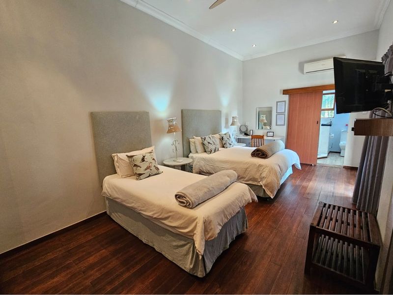 A well-maintained bedroom featuring rich hardwood flooring, recessed ceiling lighting, a wall-mounted air conditioning unit, and an en-suite bathroom access via a sliding door.